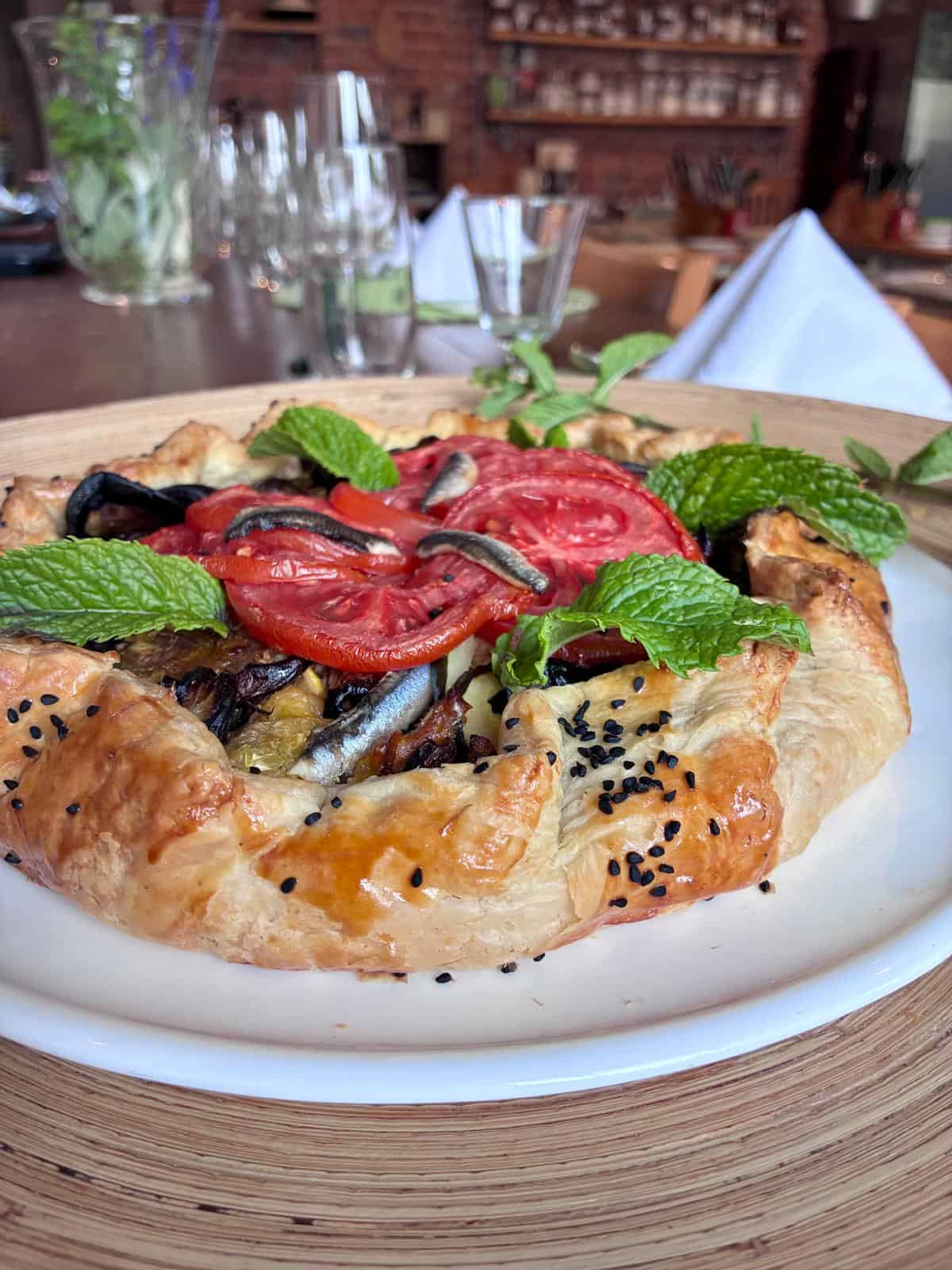 A mediterranean inspired Ratatouille Galette piled with colourful vegetables at a table set for dinner in a cookery school.
